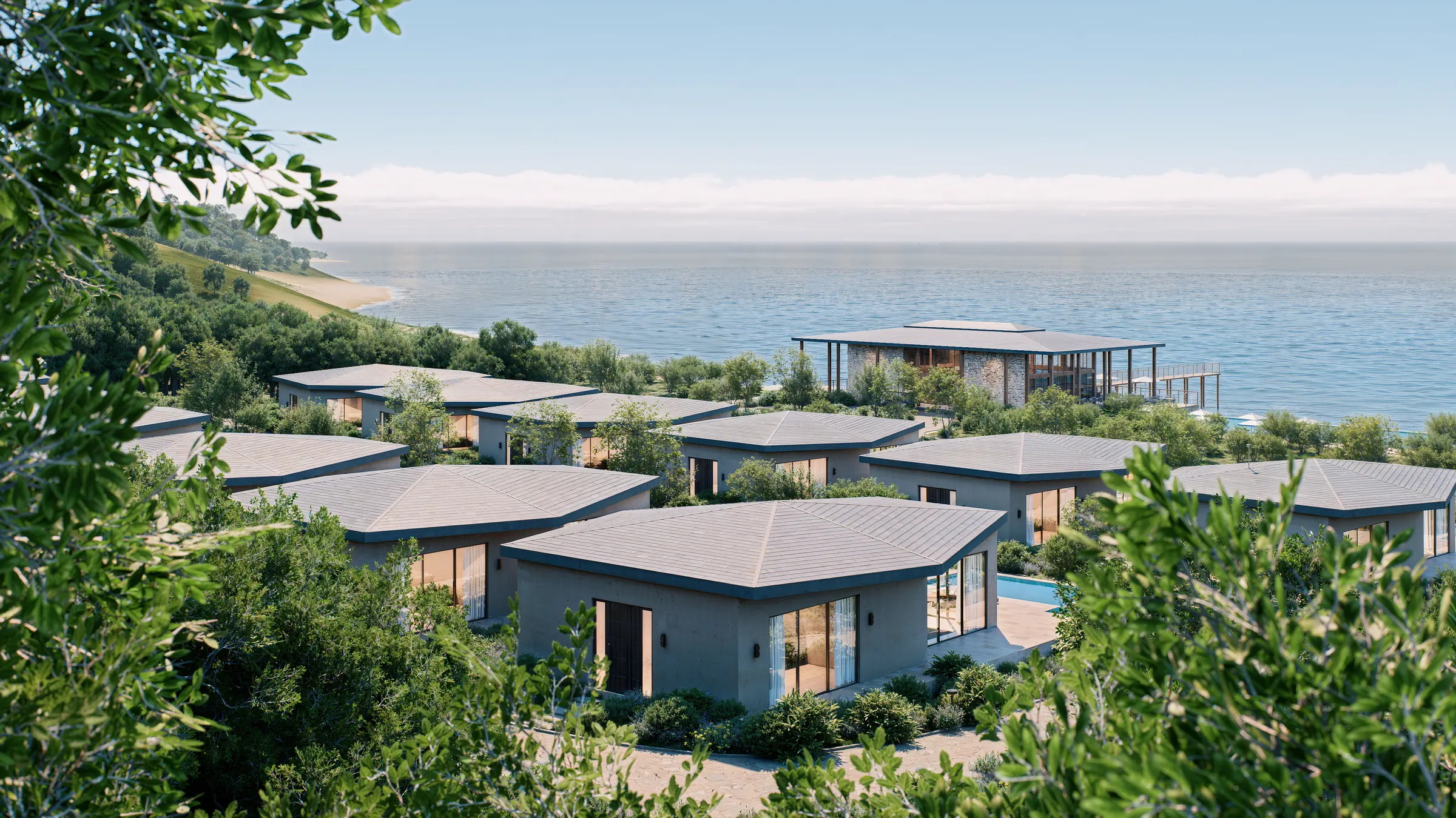 Aerial view of a coastal villa resort on a wooded hillside above the sea