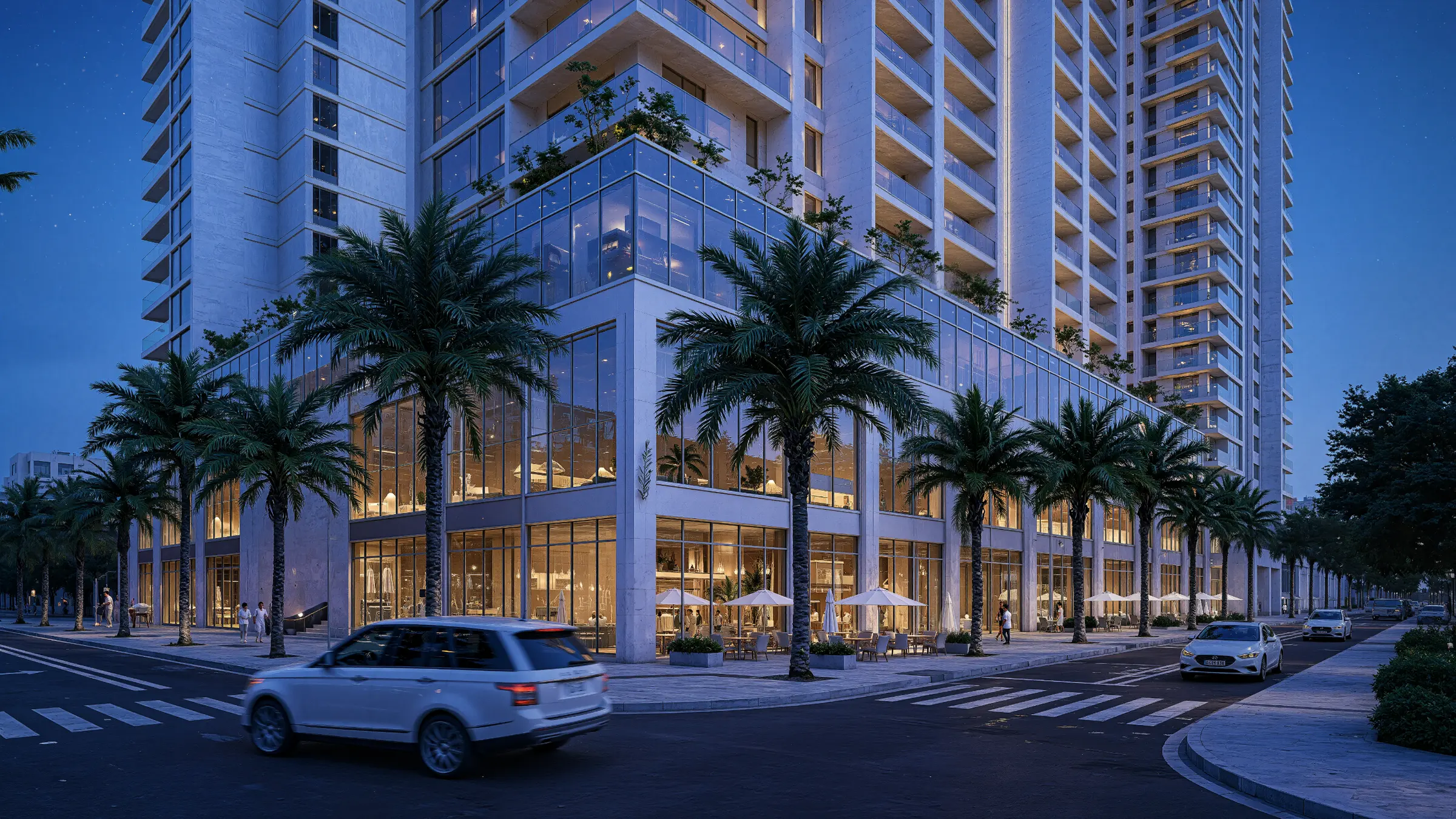 Residential tower with lit retail frontage on a palm-lined street at dusk